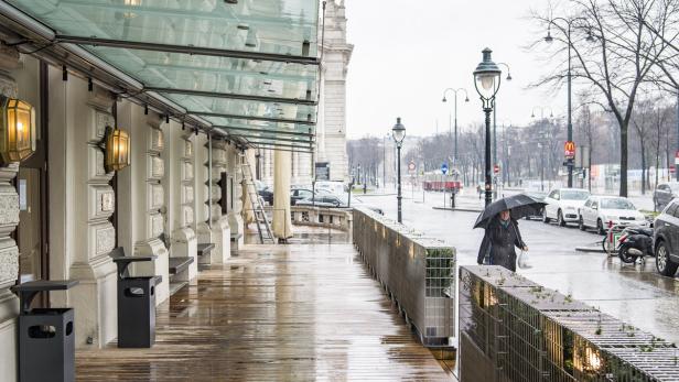 Eine Frau mit Regenschirm geht an einem regnerischen Tag in Wien die Straße entlang.