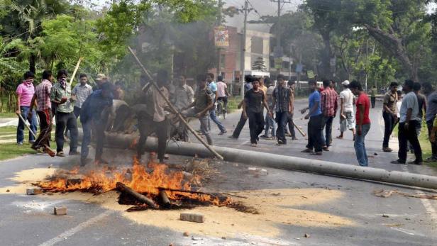 Eine Gruppe von Menschen steht auf einer Straße, auf der ein Feuer brennt und eine Betonstange liegt.