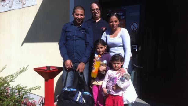 Eine Familie steht vor einem Gebäude und lächelt in die Kamera.