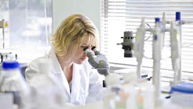 Eine Wissenschaftlerin in einem Labor, die durch ein Mikroskop blickt.