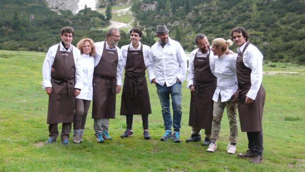 Eine Gruppe Köche steht auf einer Wiese vor einer Berglandschaft.