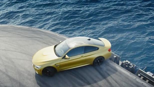 Ein goldener BMW steht auf einer Plattform mit dem Meer im Hintergrund.