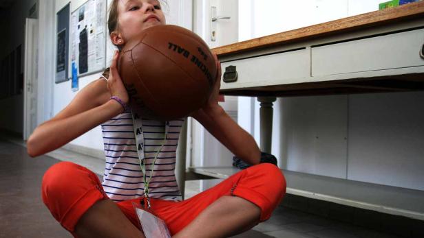 Ein Mädchen sitzt mit einem Medizinball im Arm auf dem Boden.