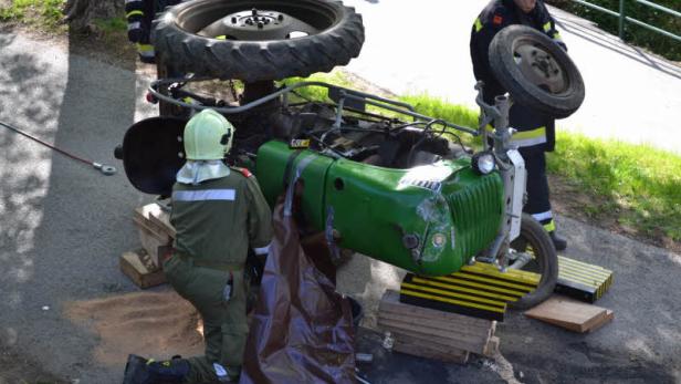 Ein umgestürzter grüner Traktor wird von Feuerwehrleuten untersucht.