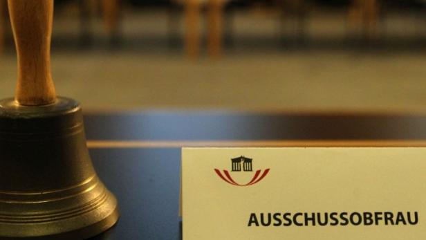Eine Glocke und ein Schild mit der Aufschrift „Ausschussobfrau“ auf einem Tisch.