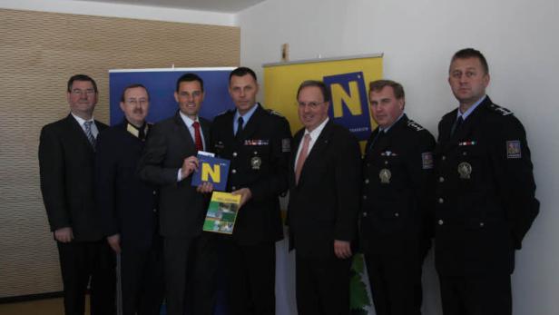 Eine Gruppe von Männern in Anzügen und Uniformen posiert für ein Foto vor einem Banner.