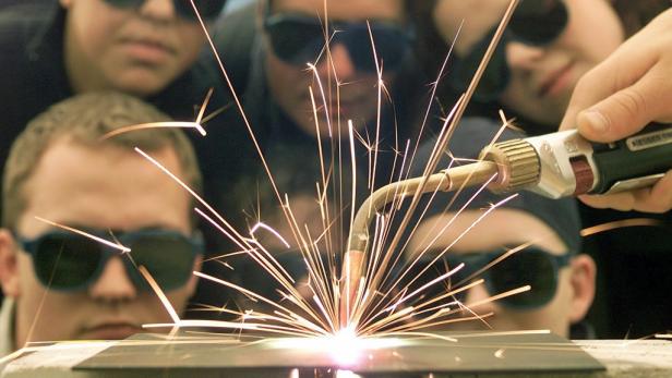 Mehrere Personen mit Schutzbrillen beobachten das Schweißen mit Funkenflug.