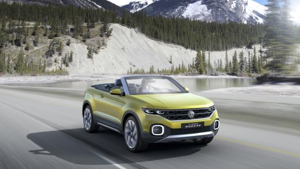 Ein gelbes VW T-Cross Breeze Cabriolet fährt auf einer Straße vor einer Berglandschaft.