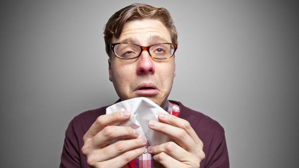 Mann mit Grippe niest in ein Taschentuch