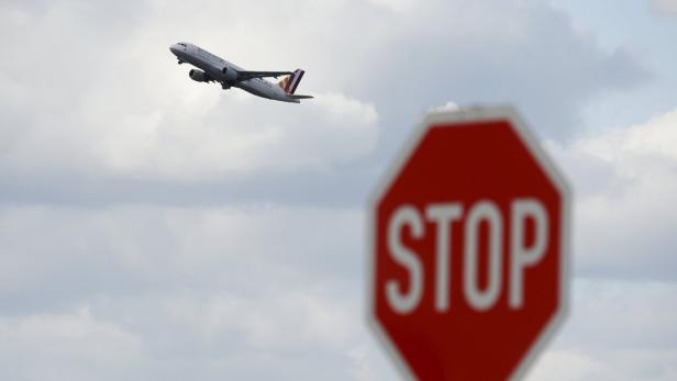 Ein Flugzeug startet vor einem bewölkten Himmel, im Vordergrund ein unscharfes Stoppschild.