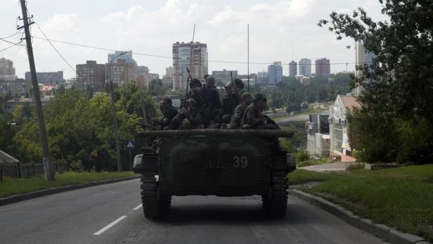 Soldaten fahren auf einem Panzer durch eine Stadt.