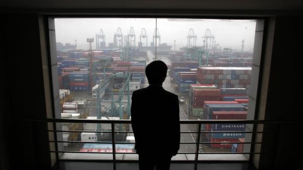 Eine Silhouette einer Person blickt aus dem Fenster auf einen Containerhafen.