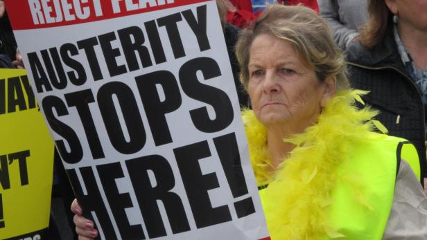 Eine Frau demonstriert mit einem Schild, auf dem „Austerity Stops Here!“ steht.