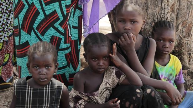 Vier afrikanische Mädchen sitzen vor einem Baum.