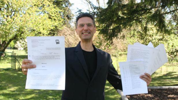 Ein Mann im Anzug hält lächelnd Dokumente in einem Garten.