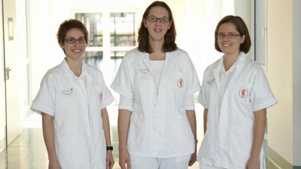 Drei Krankenschwestern stehen in einem hellen Krankenhausflur.