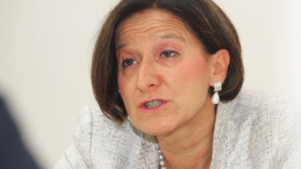 Eine Frau mit kurzem, braunem Haar und Ohrringen spricht.