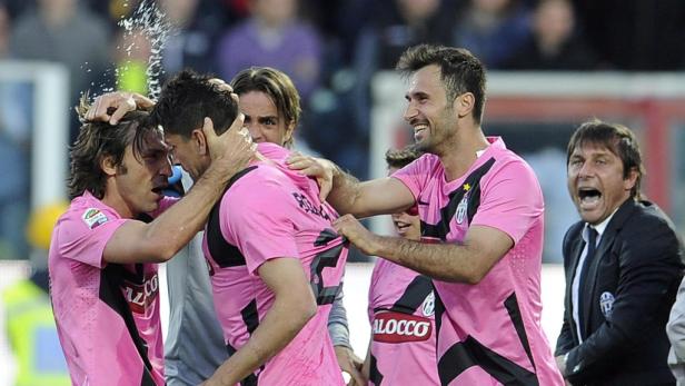 Mehrere Fußballspieler in pinkfarbenen Trikots feiern ein Tor, während ein Trainer am Spielfeldrand jubelt.