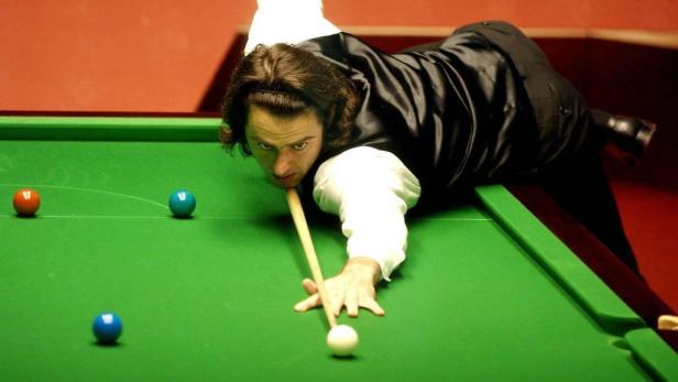 Ein Snookerspieler zielt mit dem Queue auf eine weiße Kugel.