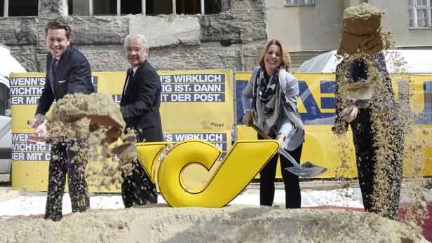 Mehrere Personen beim Spatenstich mit einem gelben Post-Logo im Vordergrund.