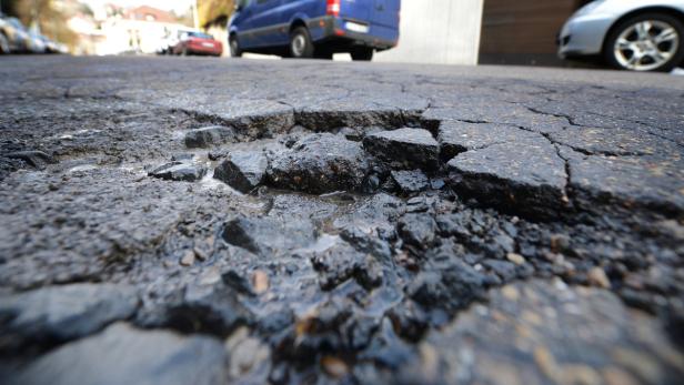 Ein Schlagloch in einer asphaltierten Straße mit stehendem Wasser.