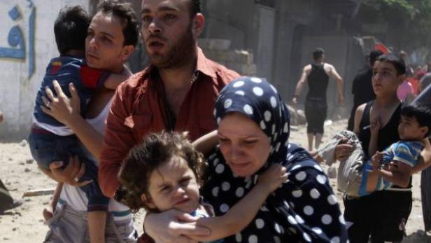 Eine Gruppe von Menschen, darunter Frauen und Kinder, geht durch eine zerstörte Gegend.