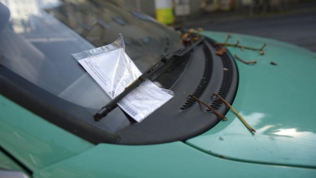 Ein Strafzettel befindet sich unter dem Scheibenwischer eines grünen Autos.