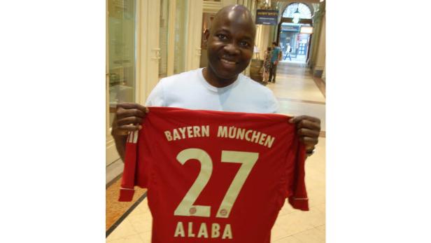 Ein Mann hält ein rotes Bayern München Trikot mit der Nummer 27 und dem Namen Alaba hoch.