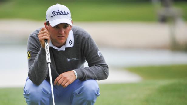 Ein Golfspieler kauert auf dem Grün und zielt mit seinem Putter.