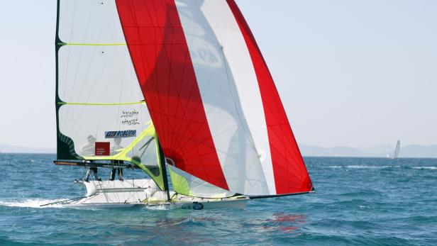 Ein Segelboot mit rot-weißen Segeln fährt auf dem Wasser.