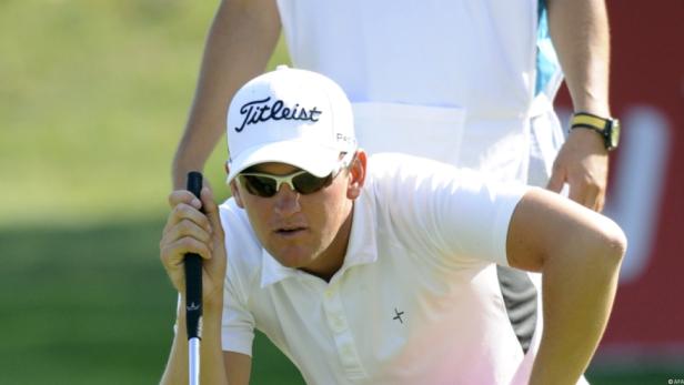 Ein Golfspieler mit Sonnenbrille und weißer Kappe zielt auf dem Grün.