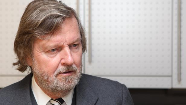 Ein Mann mit Bart und Anzug blickt nachdenklich zur Seite.