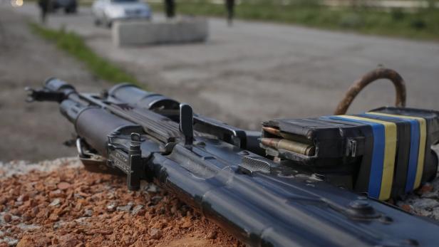Ein Maschinengewehr mit ukrainischen Farben liegt auf einem provisorischen Hindernis.