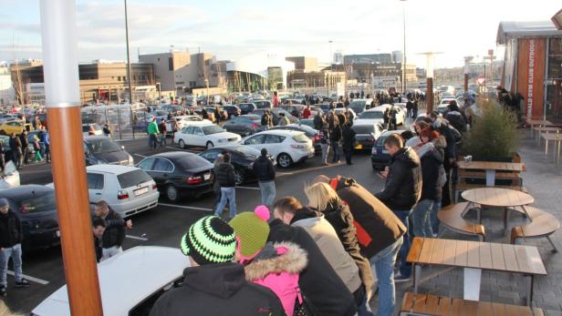 Viele Menschen versammeln sich auf einem Parkplatz mit Autos im Hintergrund.