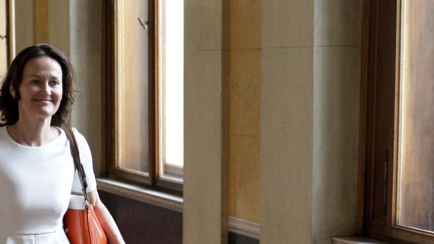 Eine Frau mit einer orangefarbenen Tasche geht einen Flur entlang.