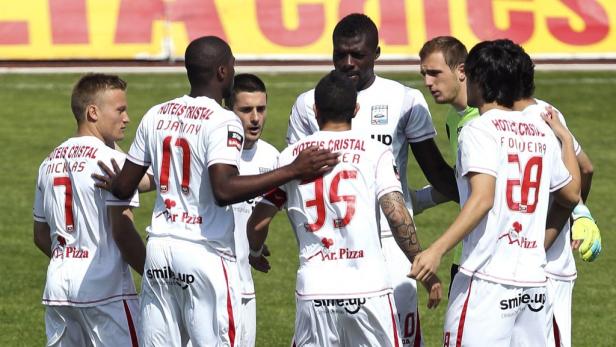 Eine Gruppe Fußballspieler in weißen Trikots umarmt sich auf dem Spielfeld.