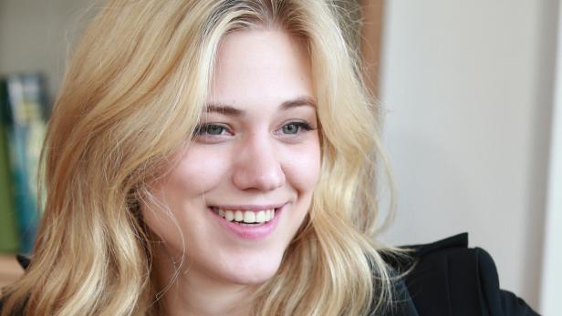 Eine lächelnde Frau mit blonden, gewellten Haaren und einem schwarzen Blazer.