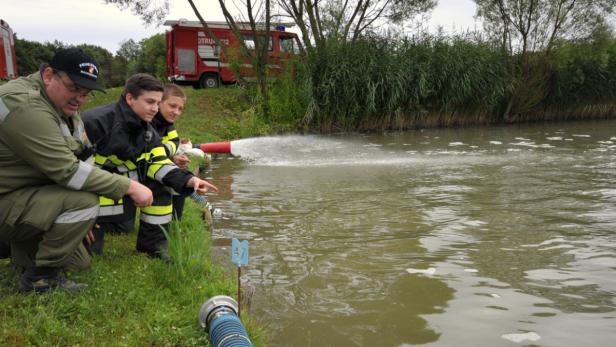 Feuerwehrleute demonstrieren die Wasserentnahme aus einem Teich mit einem Schlauch.