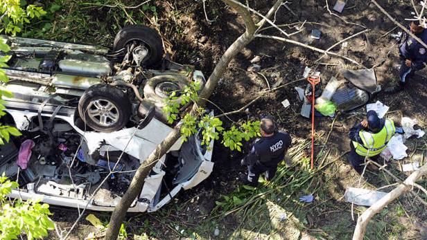 Ein schwer beschädigtes, auf dem Dach liegendes Auto wird von zwei NYPD-Beamten untersucht.