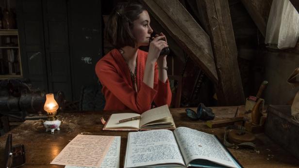 Eine junge Frau sitzt an einem Schreibtisch und trinkt aus einer Tasse, während sie von einer Lampe beleuchtet wird.