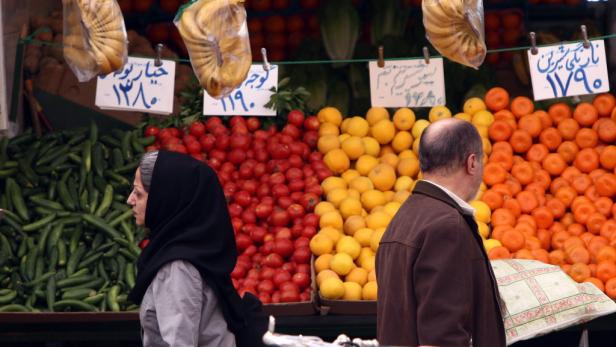 Ein Marktstand mit Obst und Gemüse, darunter Gurken, Tomaten, Zitronen und Orangen.
