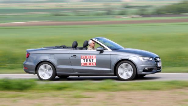 Ein graues Audi Cabriolet fährt auf einer Landstraße.