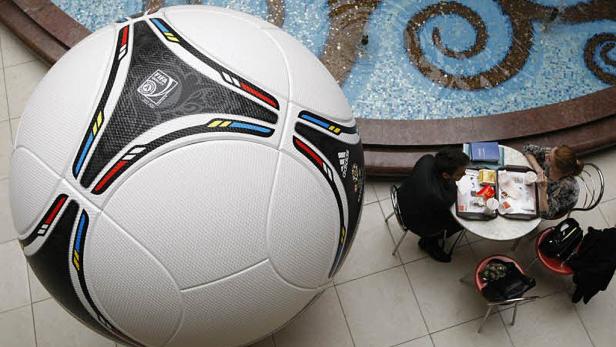 Ein übergroßer Fußball steht in der Nähe eines Tisches mit zwei Personen in einem Einkaufszentrum.