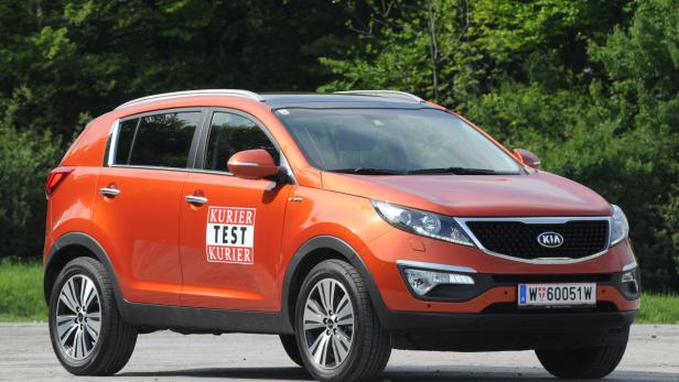 Ein orangefarbener Kia Sportage steht vor einer grünen Baumreihe.
