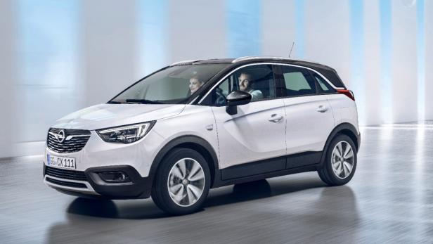 Ein weißer Opel Crossland mit zwei Personen fährt auf einer Straße.