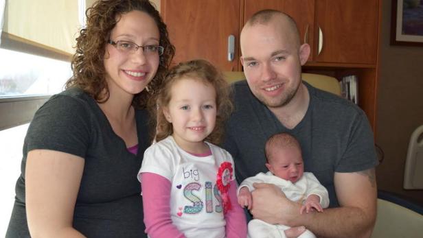 Eine Familie mit einem Neugeborenen und einem kleinen Mädchen posiert für ein Foto.