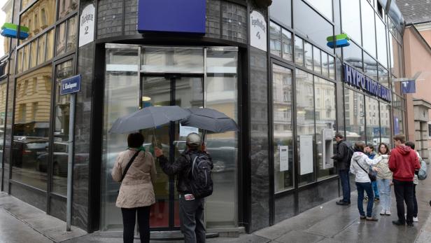 Menschen stehen mit Regenschirmen vor einer Hypo Tirol Bank Filiale.