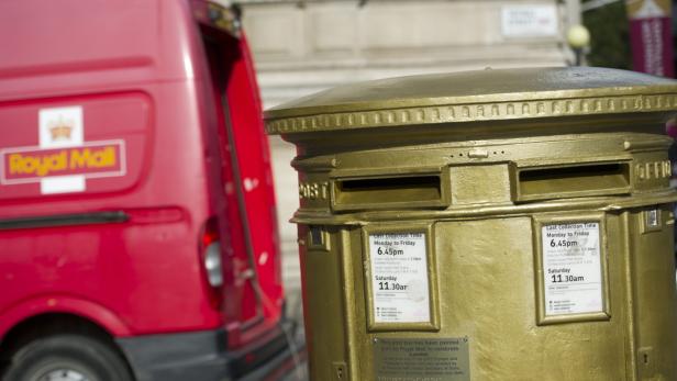 Ein goldener Briefkasten der Royal Mail neben einem roten Lieferwagen.