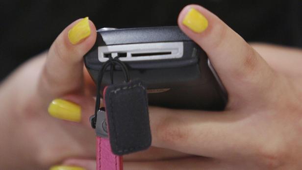 Eine Person mit gelb lackierten Nägeln hält eine schwarze Kamera in der Hand.