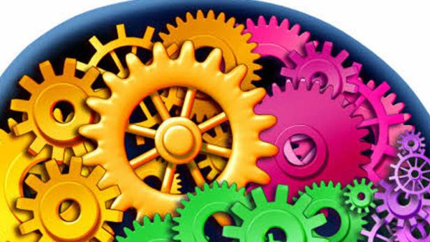 Verschiedenfarbige Zahnräder greifen ineinander und bilden ein komplexes System.